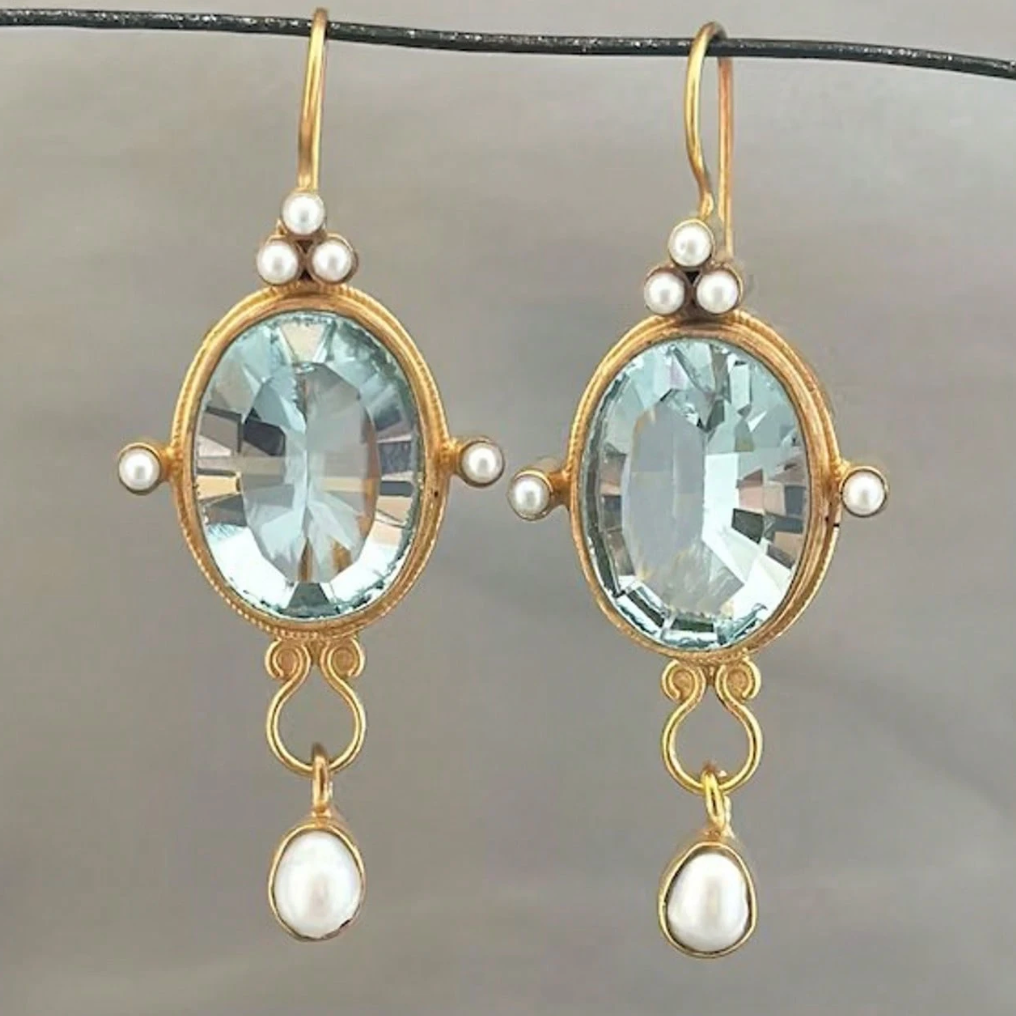 Pair of gold earrings with blue gemstones and pearl accents on a gray background