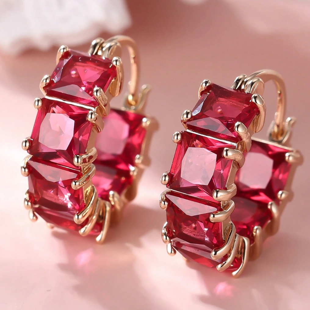 Pair of earrings with red gemstones and gold accents on a soft pink background