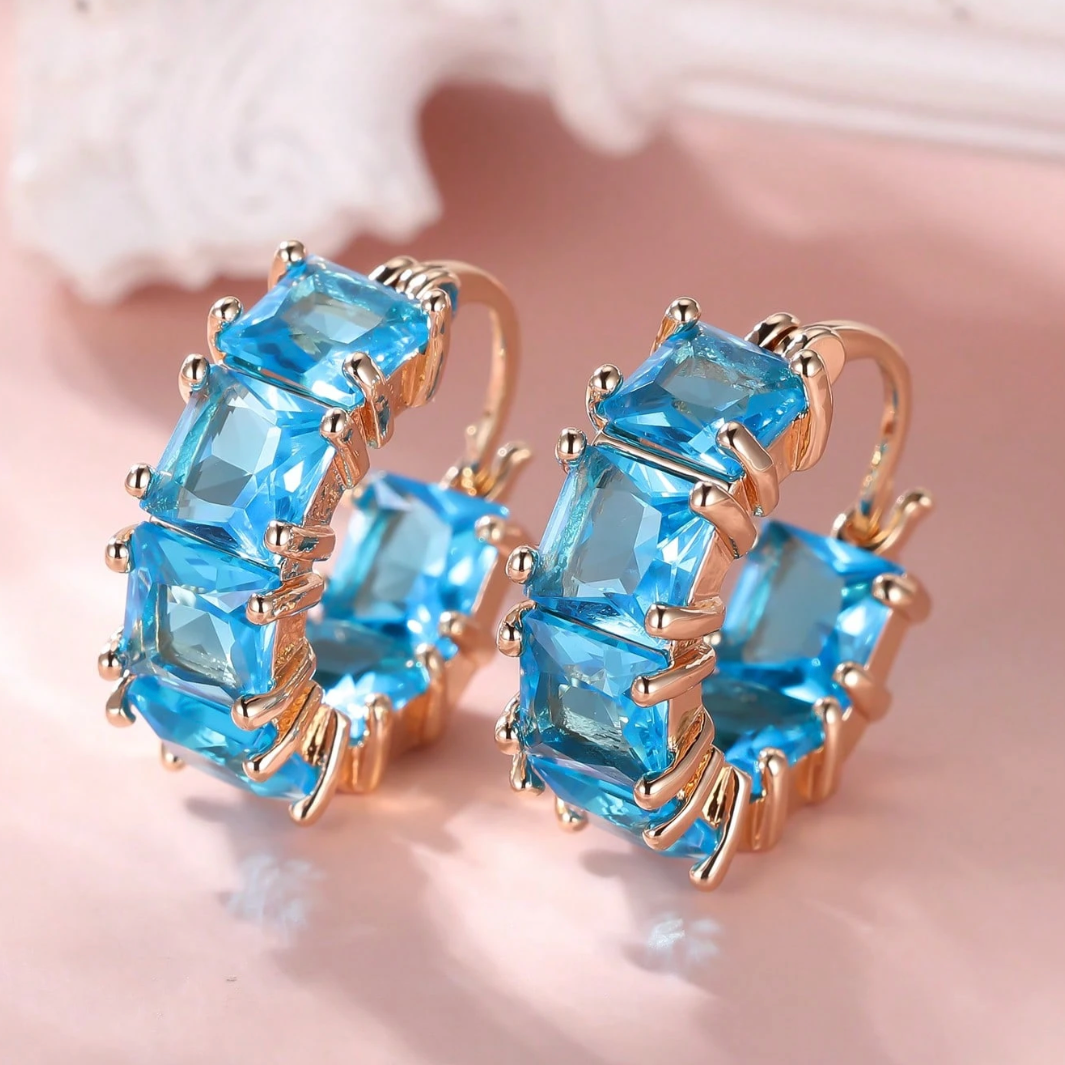 Pair of earrings with blue gemstones and gold accents on a soft pink background