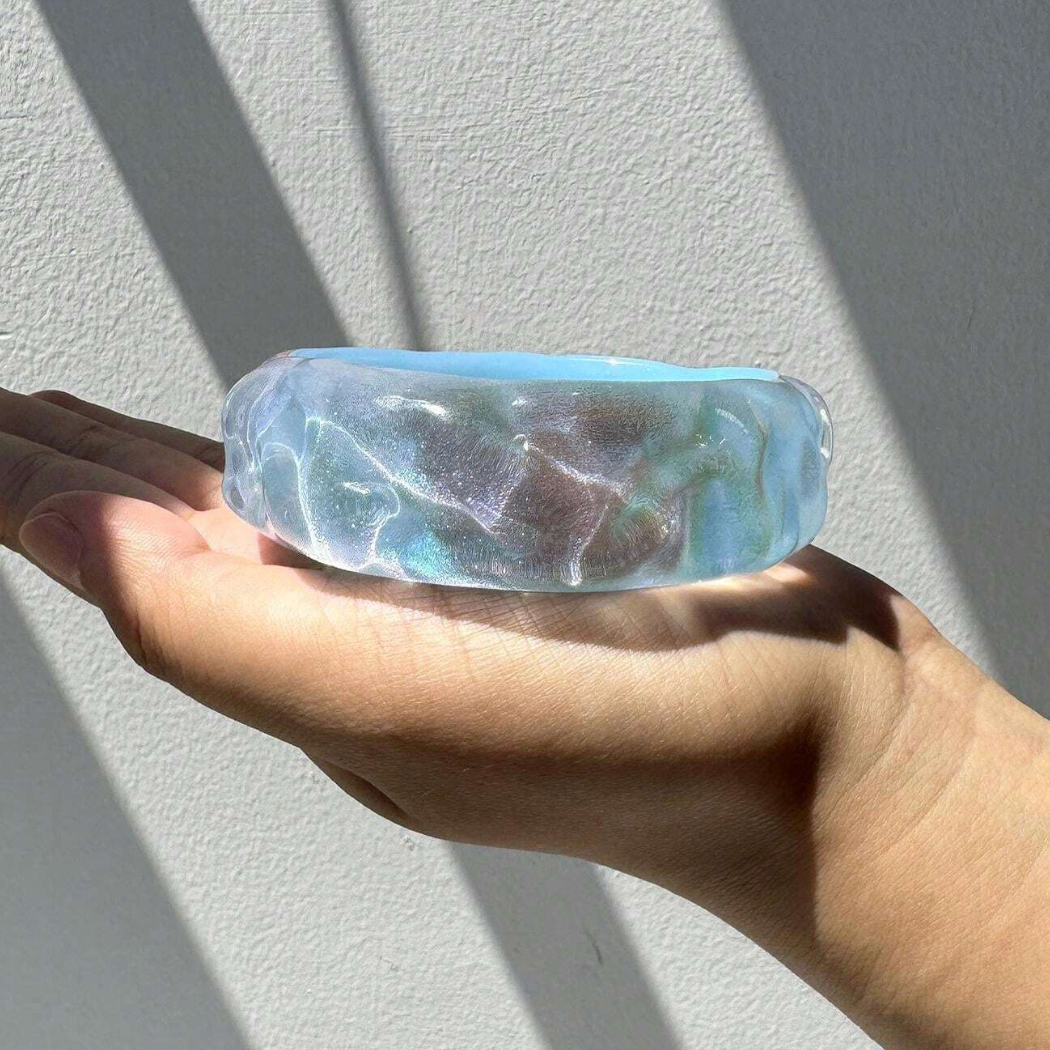 Hand holding a clear stone with blue and green marbling against a light gray background
