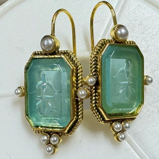 Pair of gold earrings with green gemstones and pearl accents on a white background