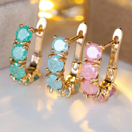 Three pairs of gold hoop earrings with gemstones on a reflective surface.
