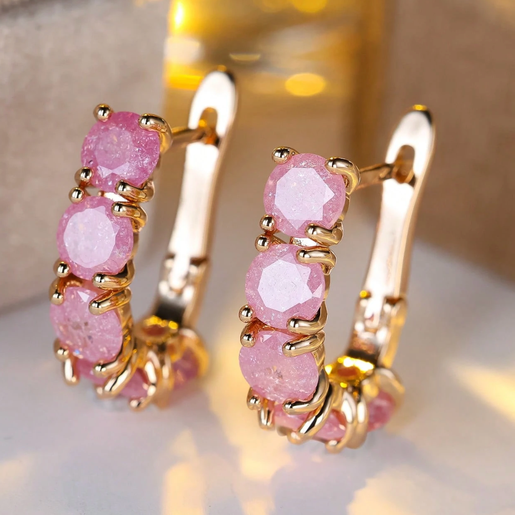 Gold hoop earrings with pink gemstones on a light background