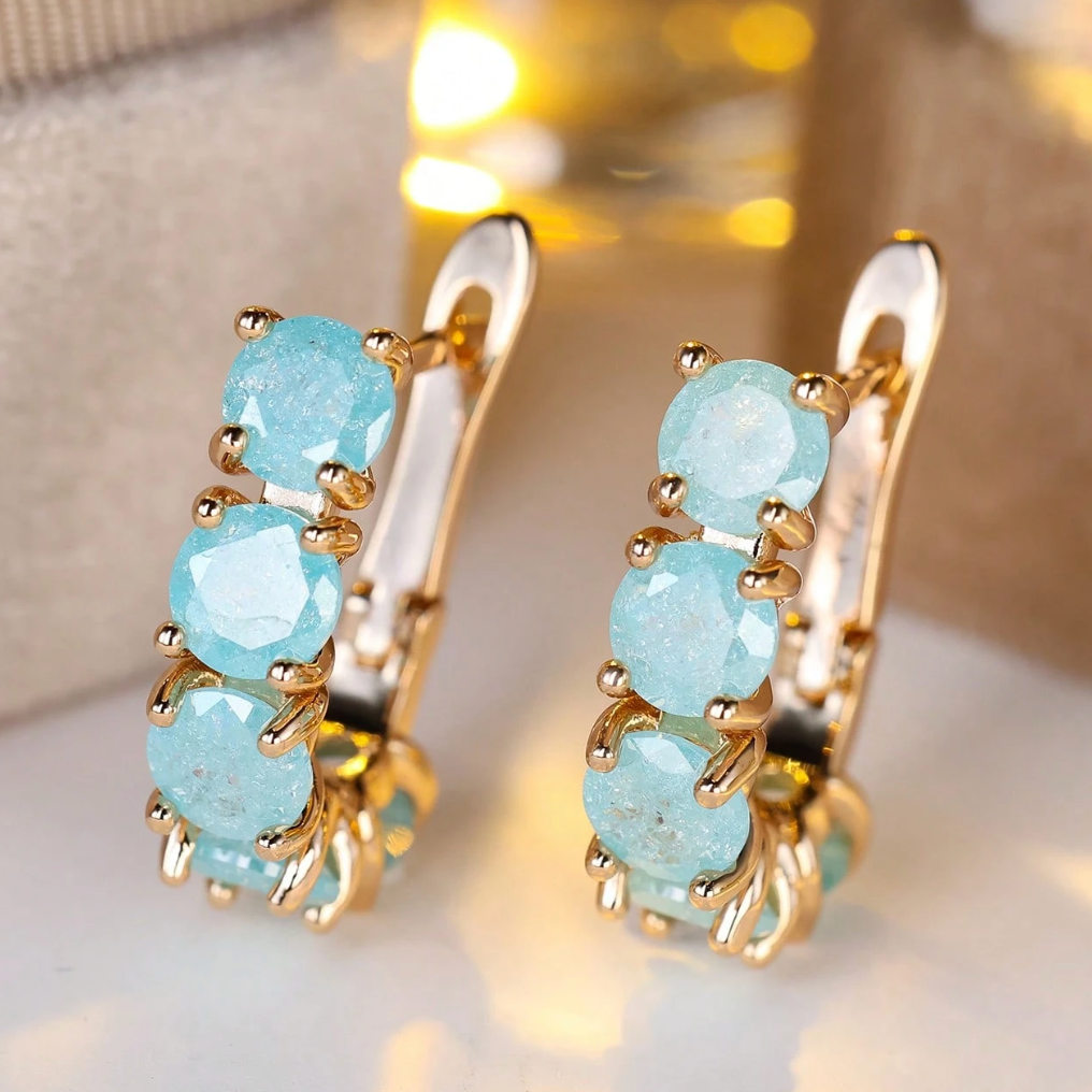 Gold earrings with light blue gemstones on a reflective surface.