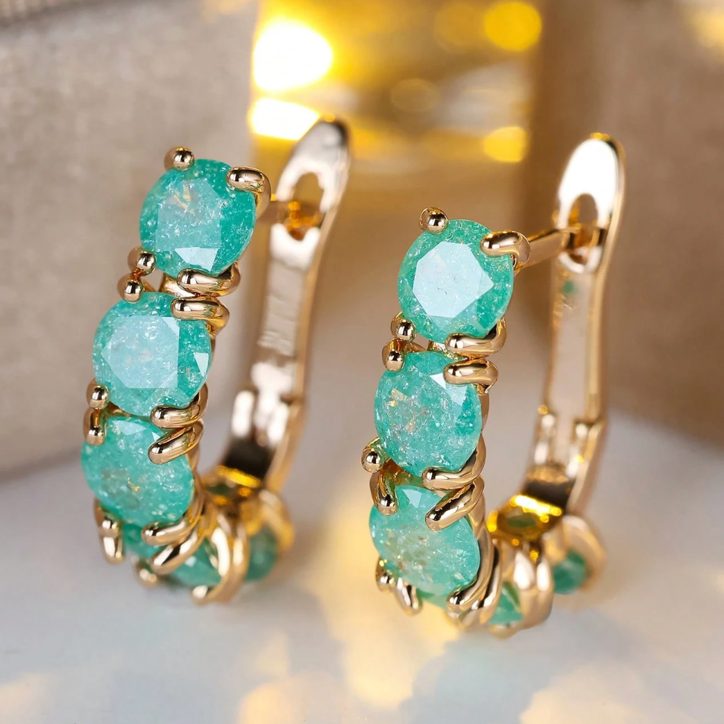 Gold hoop earrings with turquoise stones on a reflective surface.