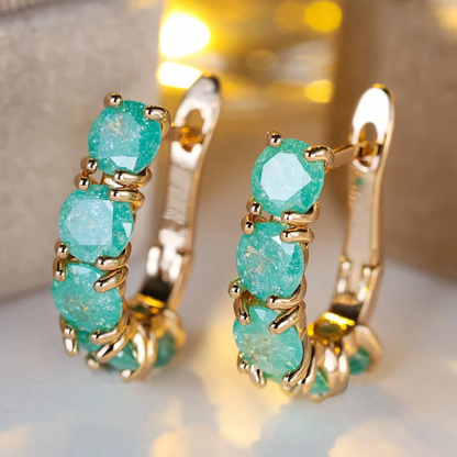 Gold hoop earrings with turquoise stones on a reflective surface.