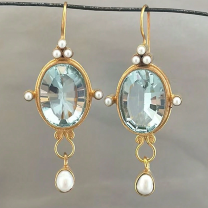 Pair of gold earrings with blue gemstones and pearl accents on a gray background