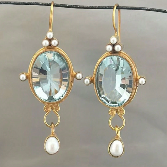 Pair of gold earrings with blue gemstones and pearl accents on a gray background