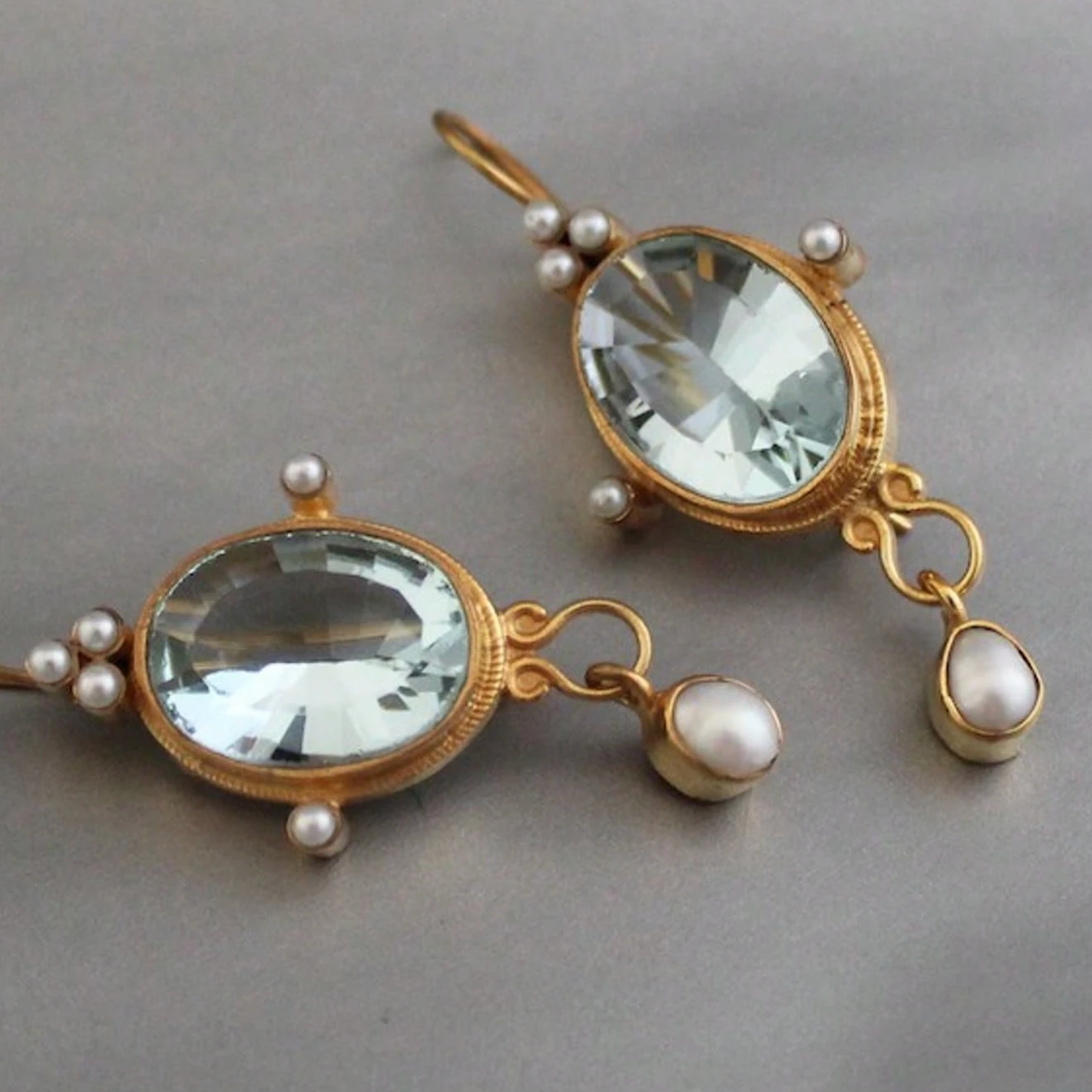 Pair of gold earrings with clear gemstones and pearls on a gray background