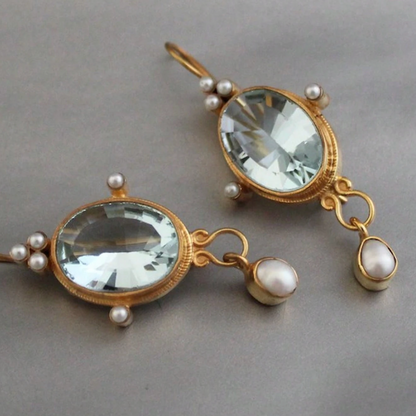 Pair of gold earrings with clear gemstones and pearls on a gray background