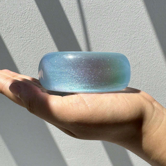 Hand holding a blue glittery bangle against a light gray background