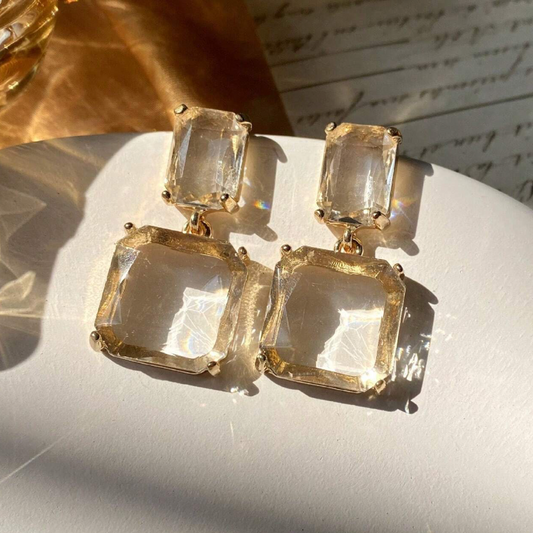 Gold earrings with clear gemstones on a light surface