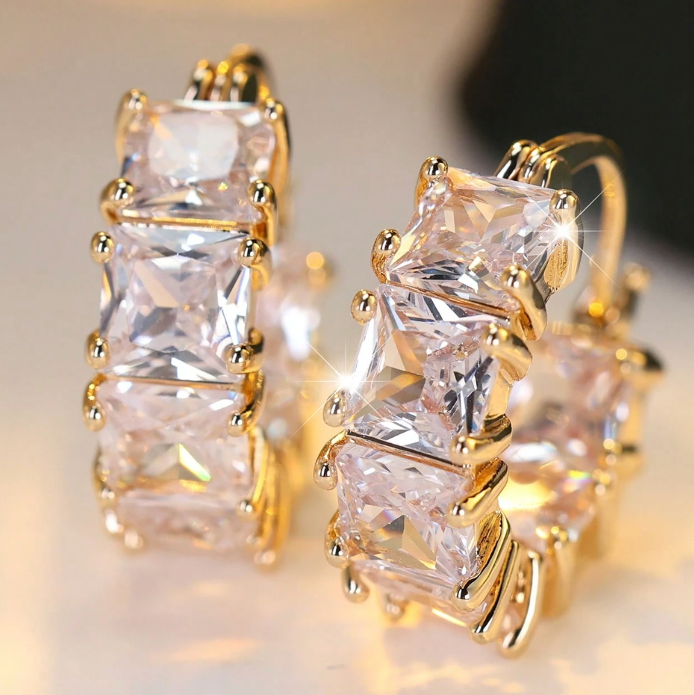 Gold hoop earrings with clear gemstones on a blurred background
