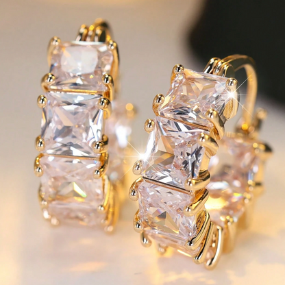Gold hoop earrings with clear gemstones on a blurred background