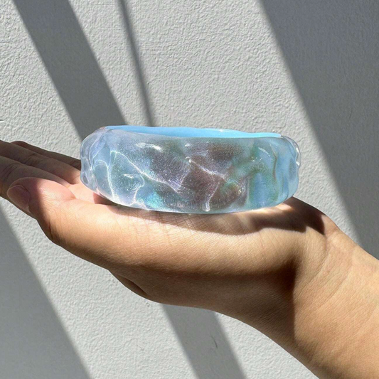 Hand holding a clear stone with blue and green marbling against a light gray background