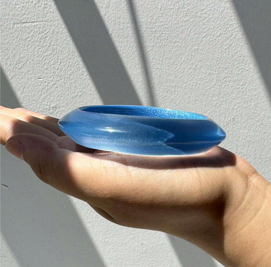 Blue glass object held in a hand against a light gray background