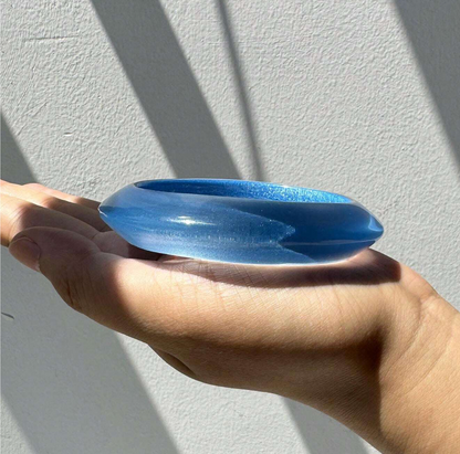 Blue glass object held in a hand against a light gray background