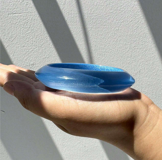 Blue glass object held in a hand against a light gray background